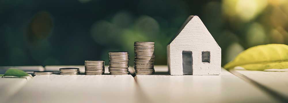 Pile of coins with a house beside them, representing saving up to buy a home