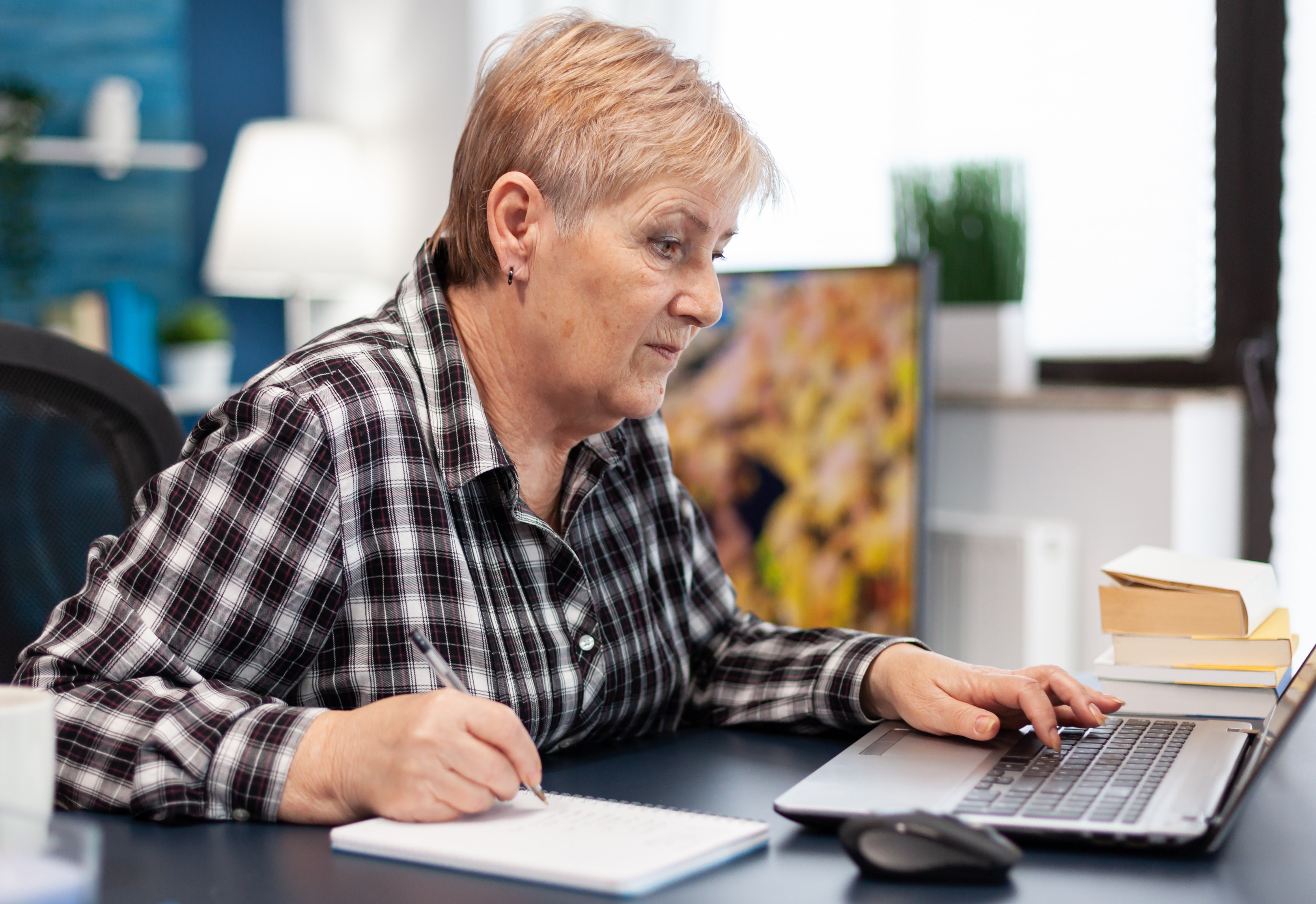 Woman checking bank balance on her laptop and writing it on a notebook