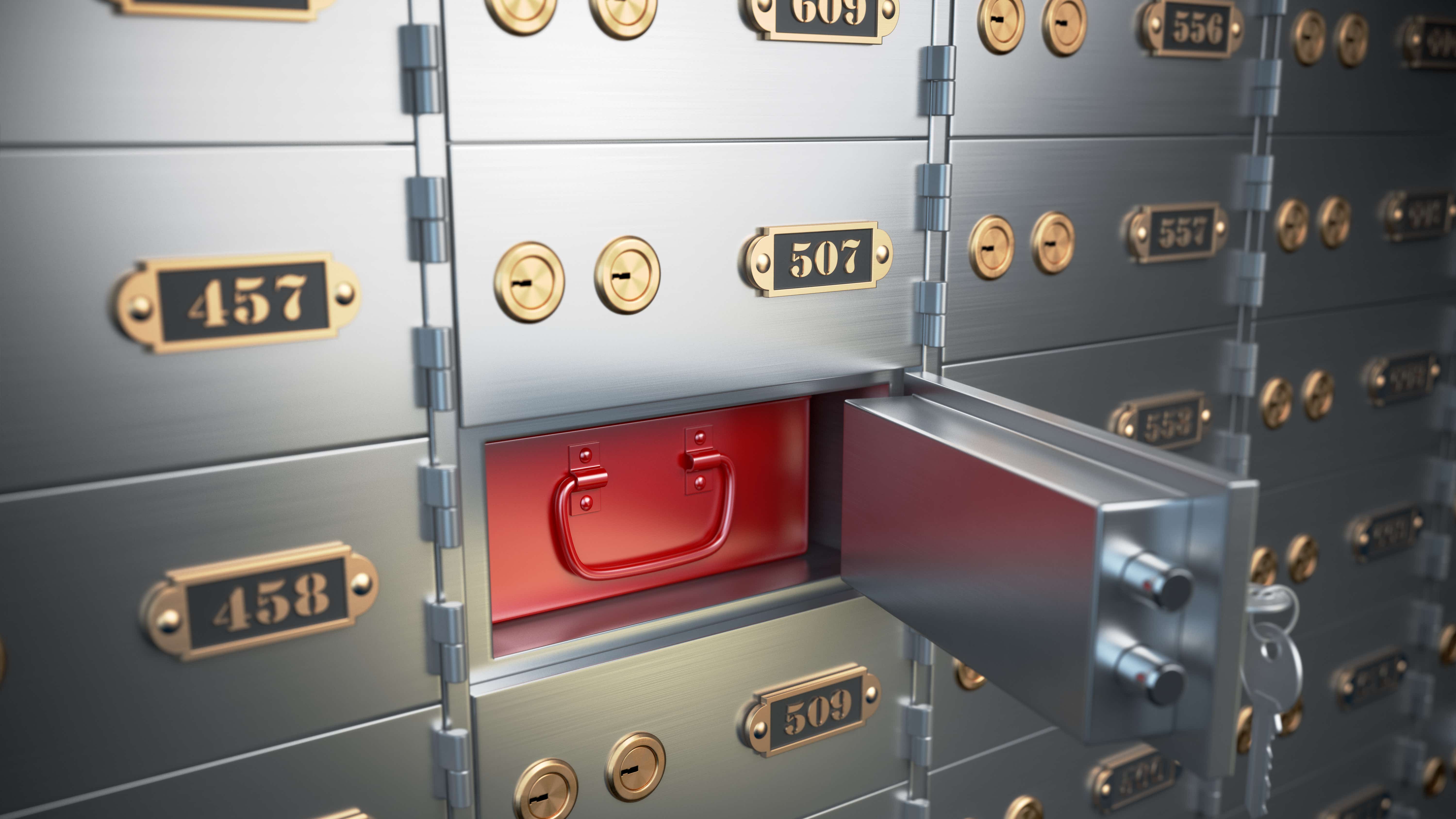 A wall full of grey, numbered safety deposit boxes, one of which is open, displaying a red metal container to secure goods
