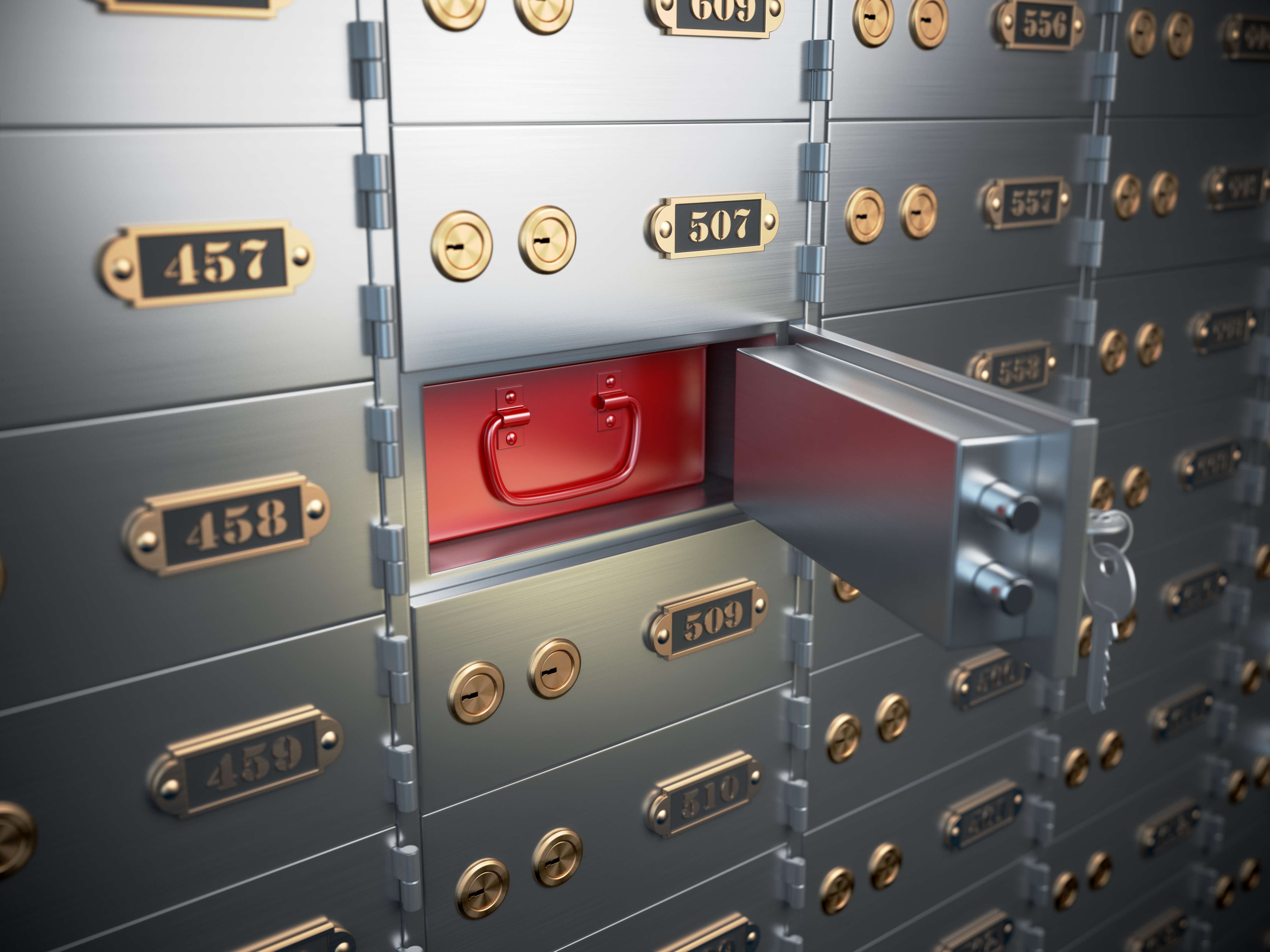 A wall full of grey, numbered safety deposit boxes, one of which is open, displaying a red metal container to secure goods 