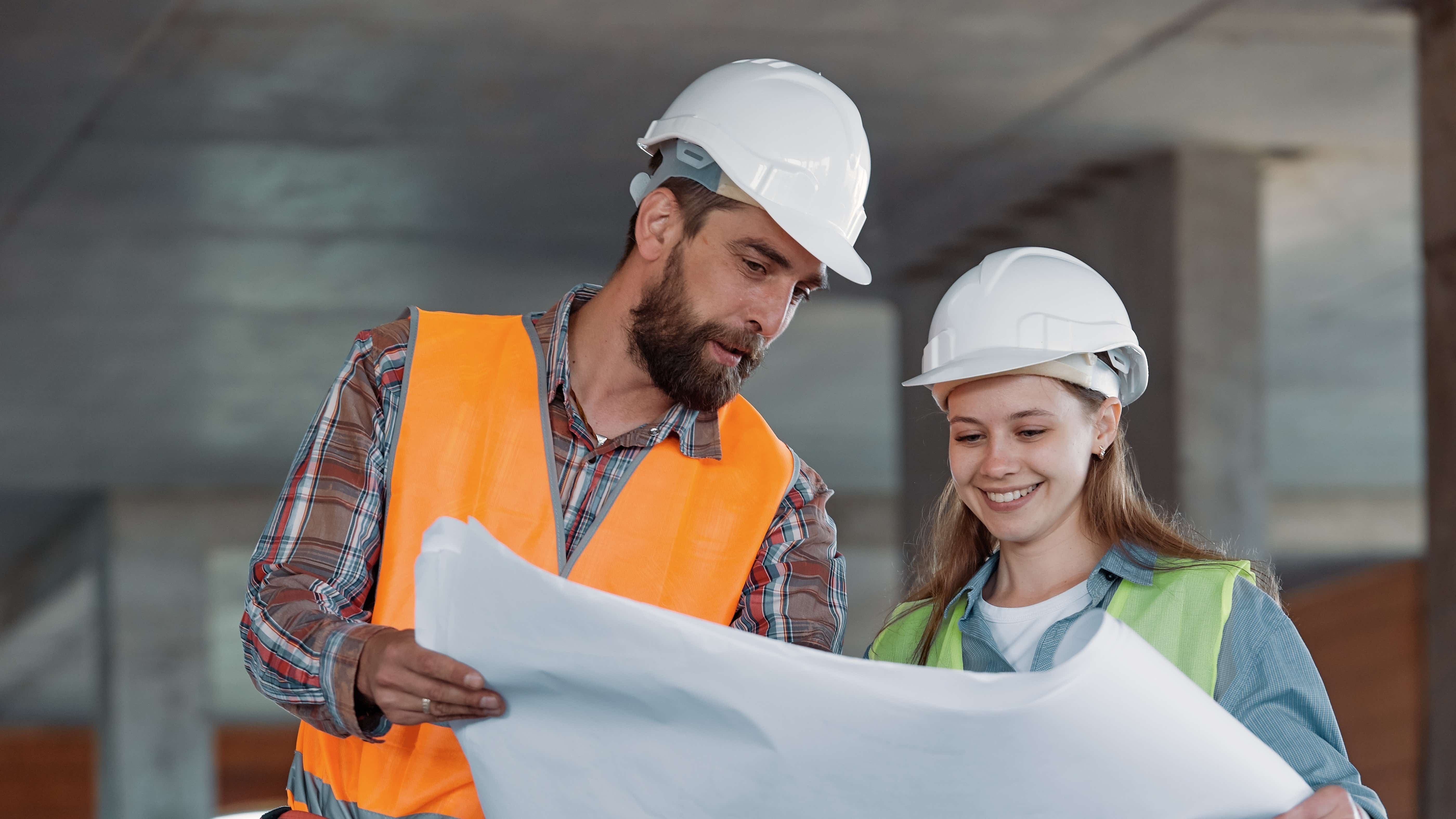 Man and woman in hard hats look at a building plan