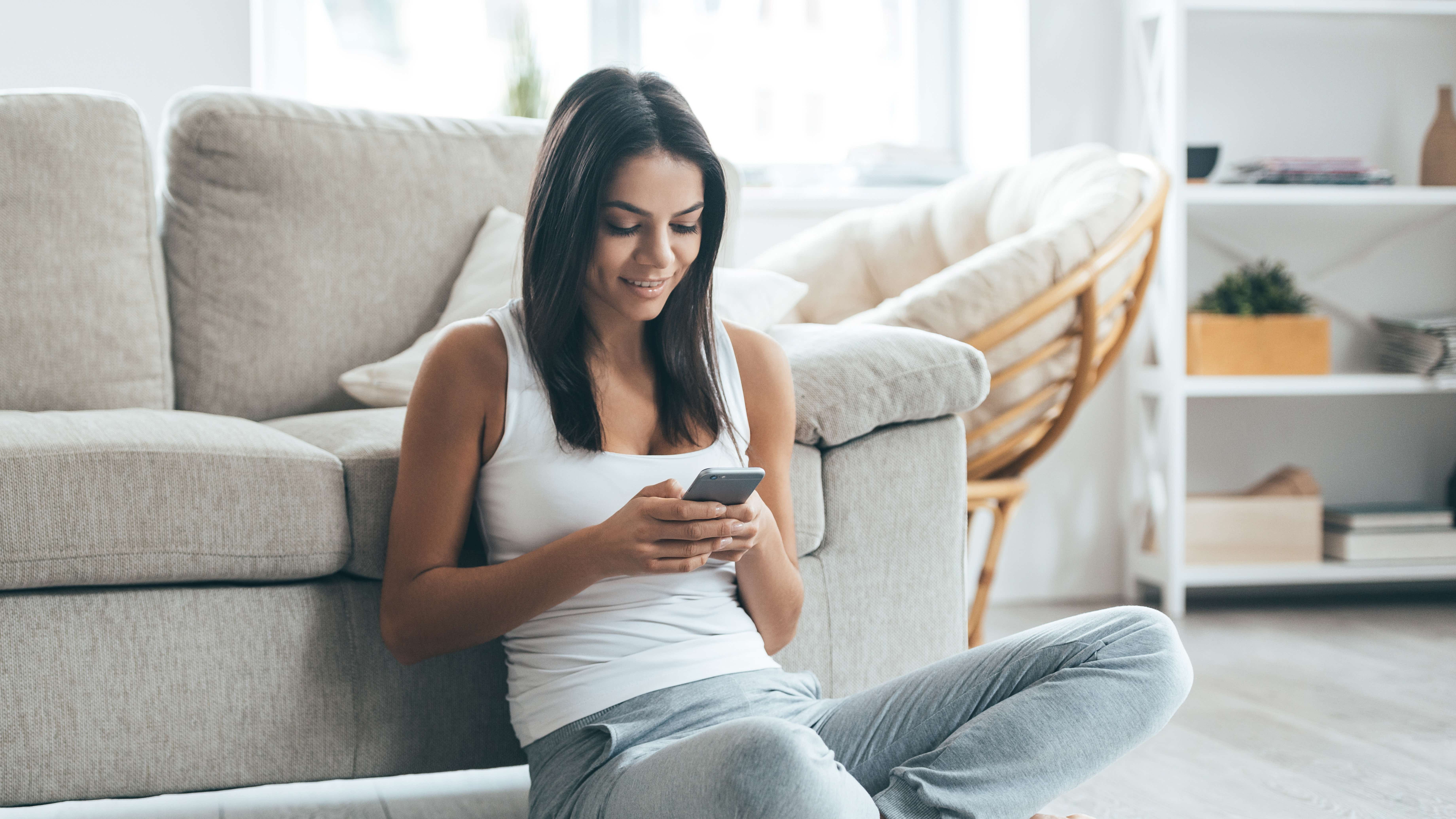 Young woman sitting on the floor at home looking at her phone