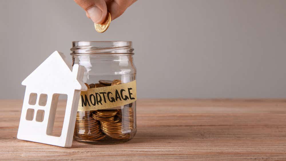 How to save for a mortgage deposit. Image of someone dropping coins in a jar labelled mortgage