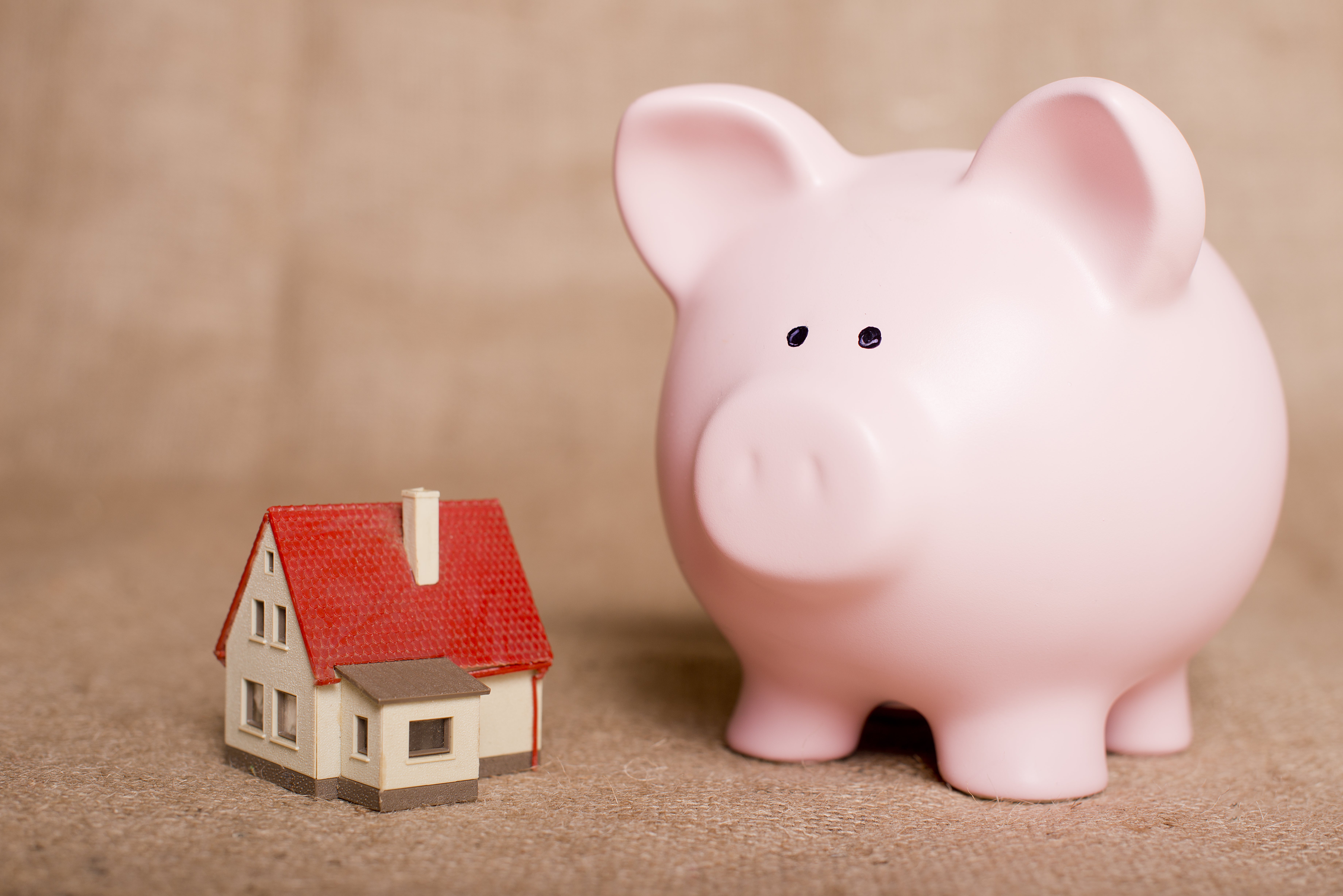 A large pink piggy bank sits on a desk next to a much smaller model of a red house