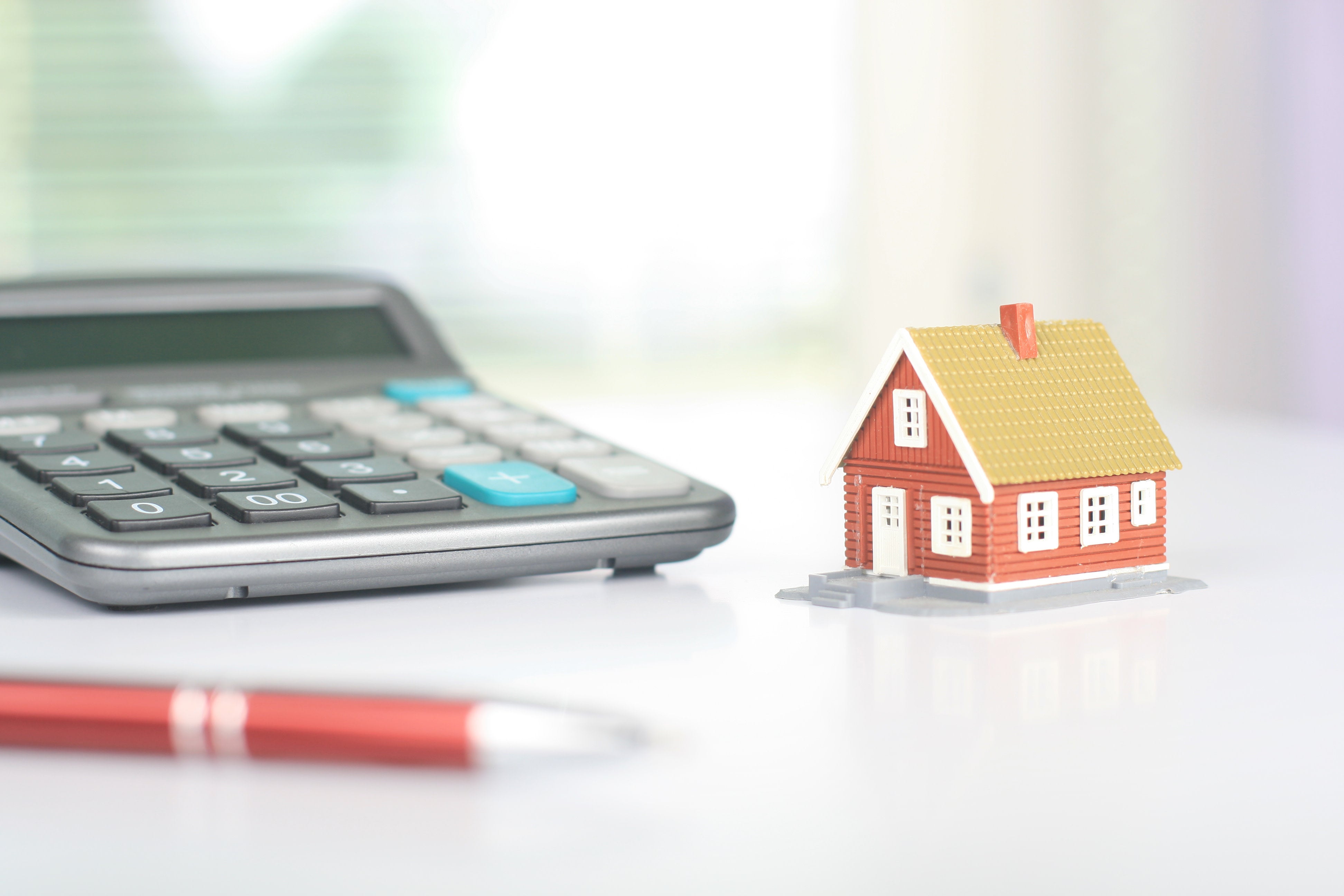 A large calculator sits on a desk next to a tiny model house