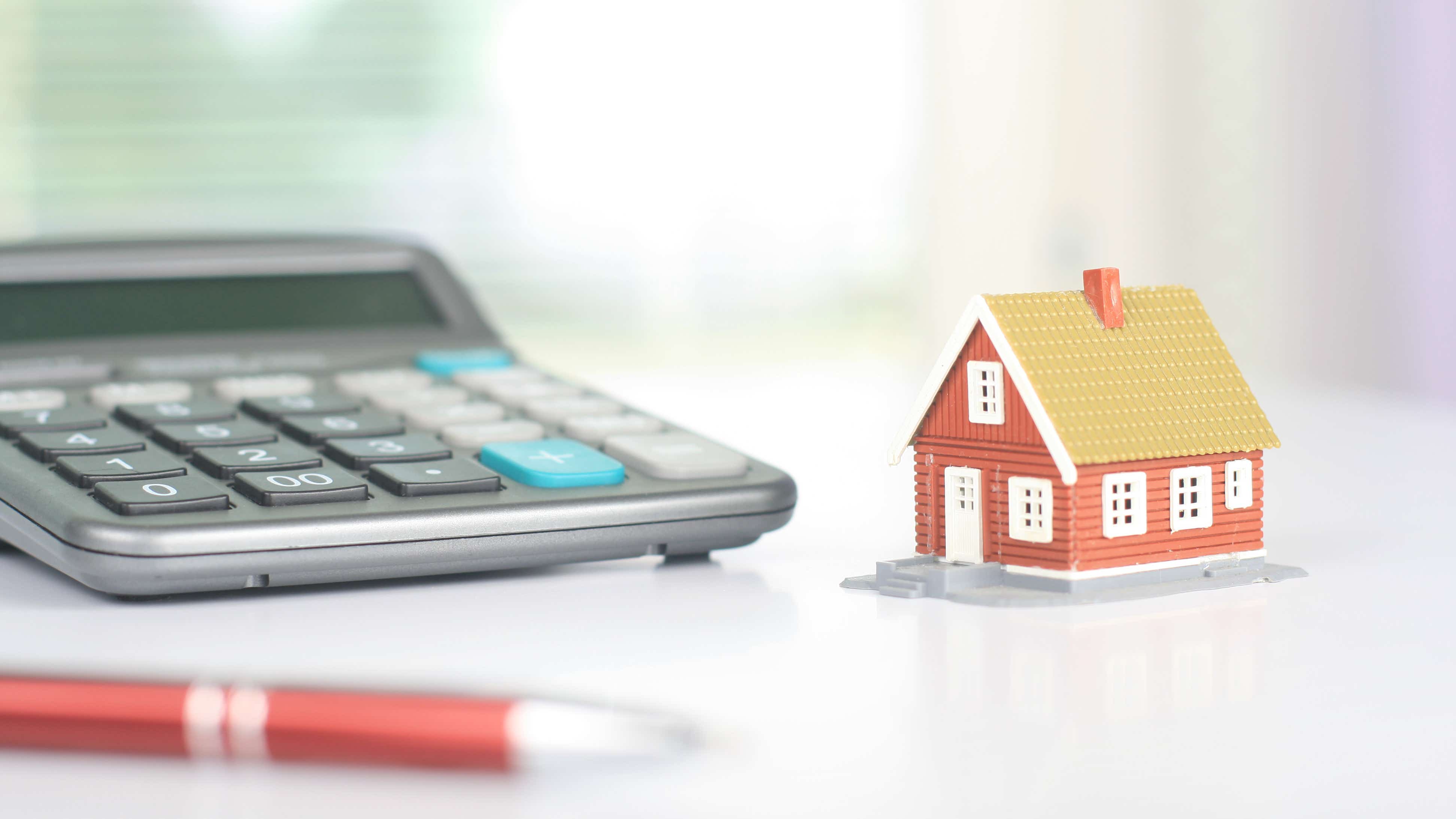 A large calculator sits on a desk next to a tiny model house