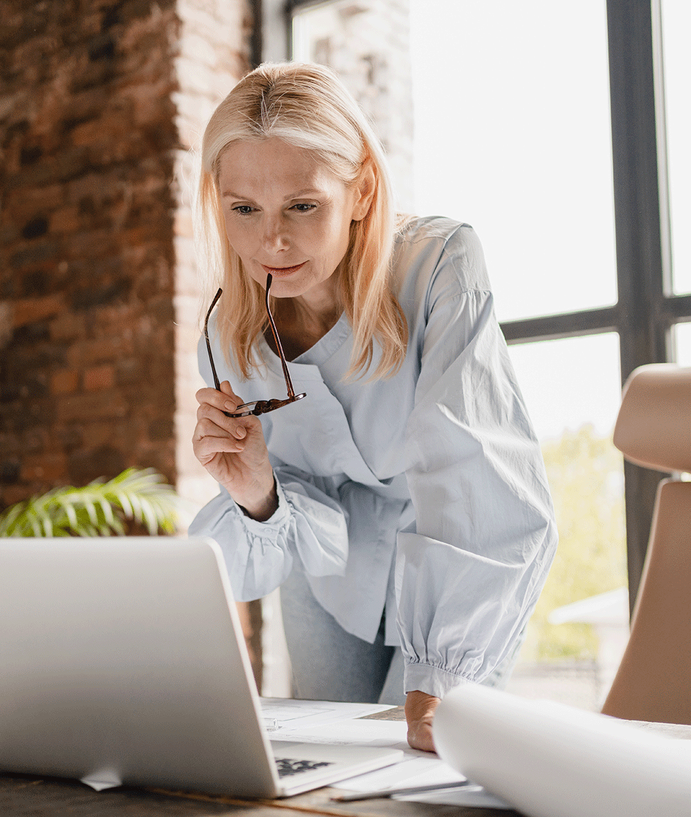Blonde woman with glasses looking at laptop thoughtfully
