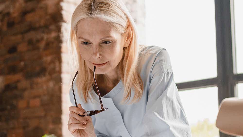 Blonde woman with glasses looking at laptop thoughtfully