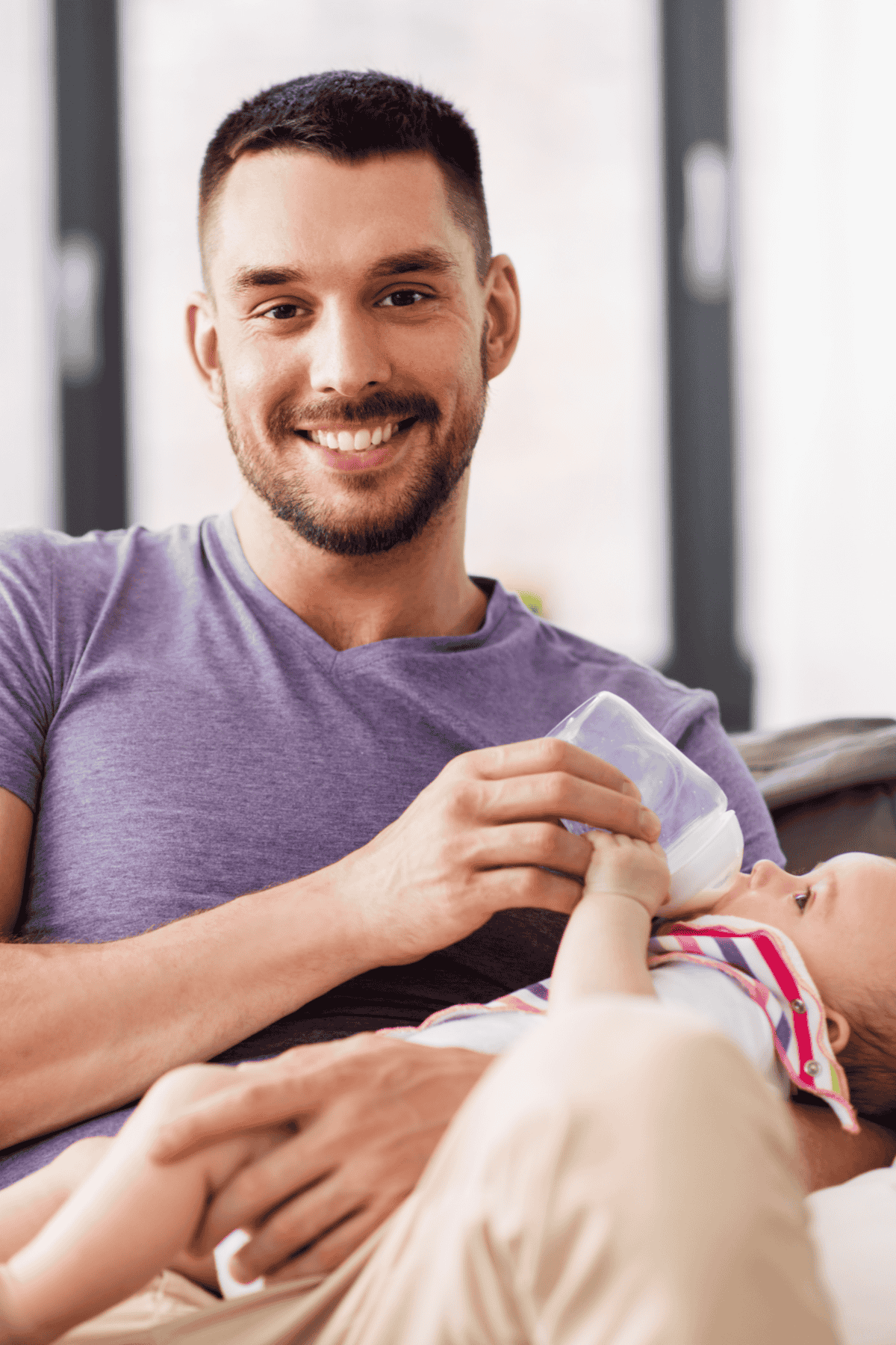 Father feeding little daughter with baby formula from bottle at home