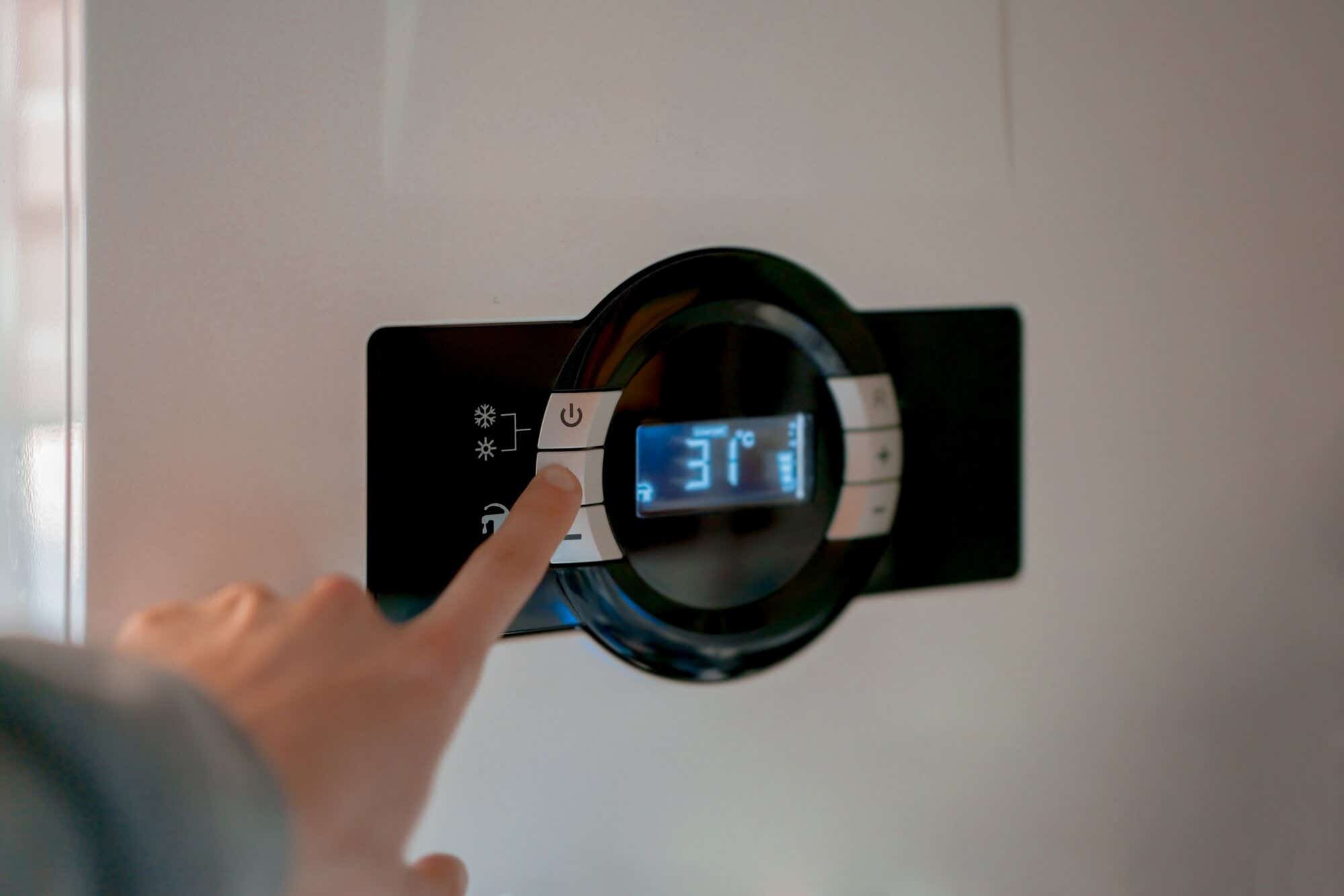 Man's hand clicks button on a front panel of gas combi boiler with 31 celsius on the display.