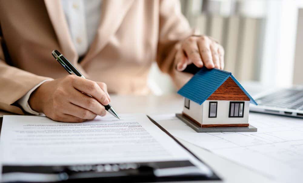 An image of a man sat beside a model home and a contract about to sign the contract.