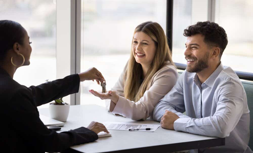 An image of a smiling couple receiving house keys from a solicitor in an office.