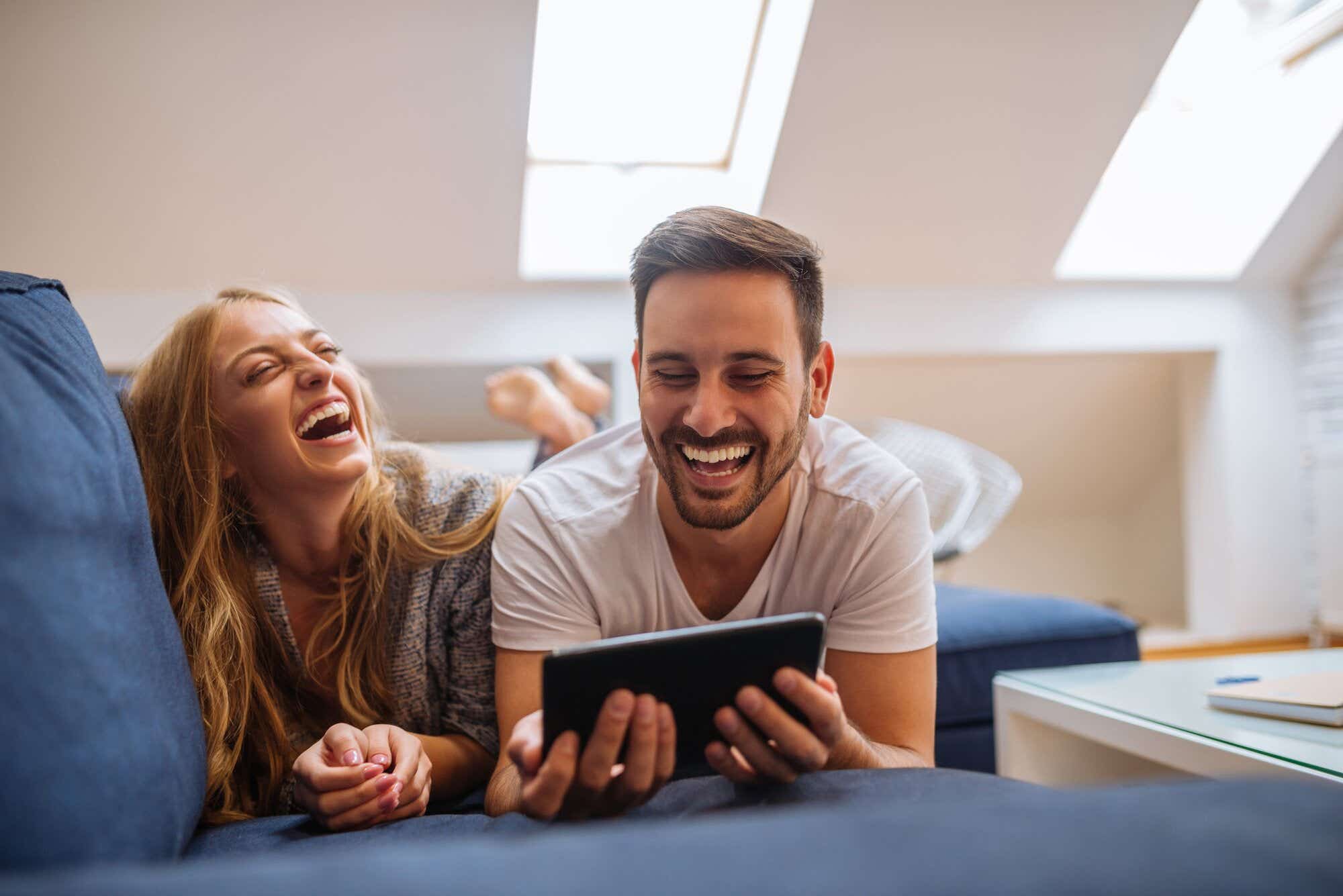 two people laughing at something they're watching on a tablet