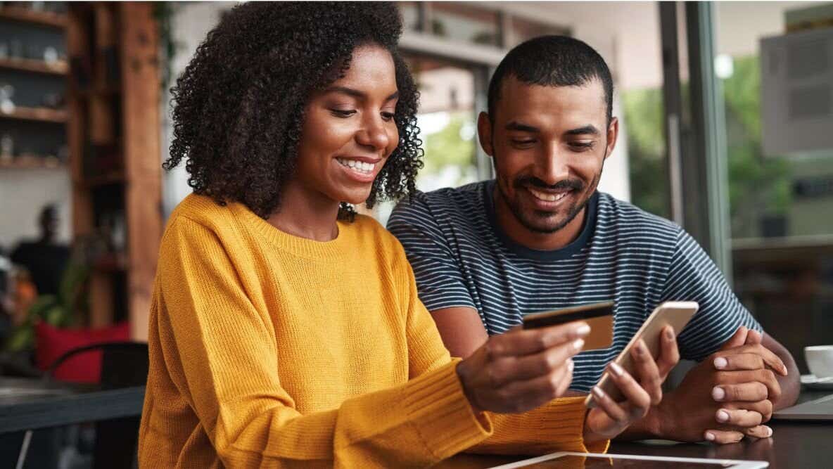 Person looking down at a phone in their hand while smiling and holding a credit card in the other hand