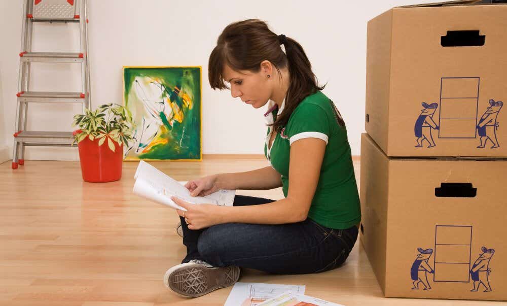 An image of a woman sitting on the floor reading instructions alongside boxes as she prepares to move house.
