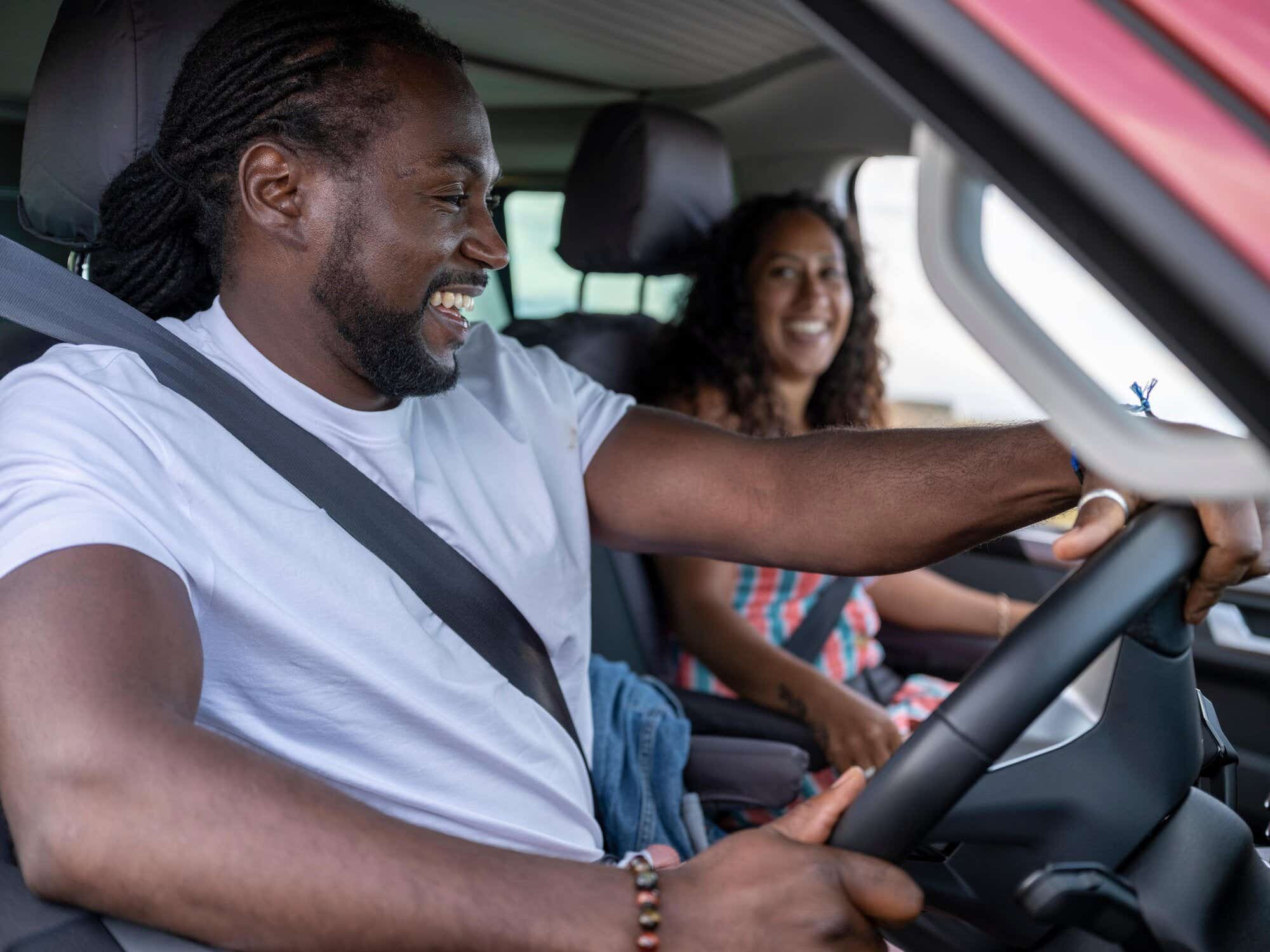 A man driving a van, smiling with a woman in the passenger seat