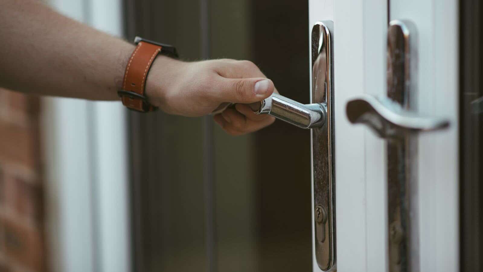 A mans hand on a door handle, opening door