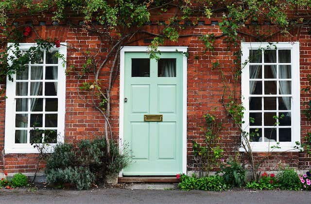 Front of a house with a light green front door, large windows either side and some plants surrounding them