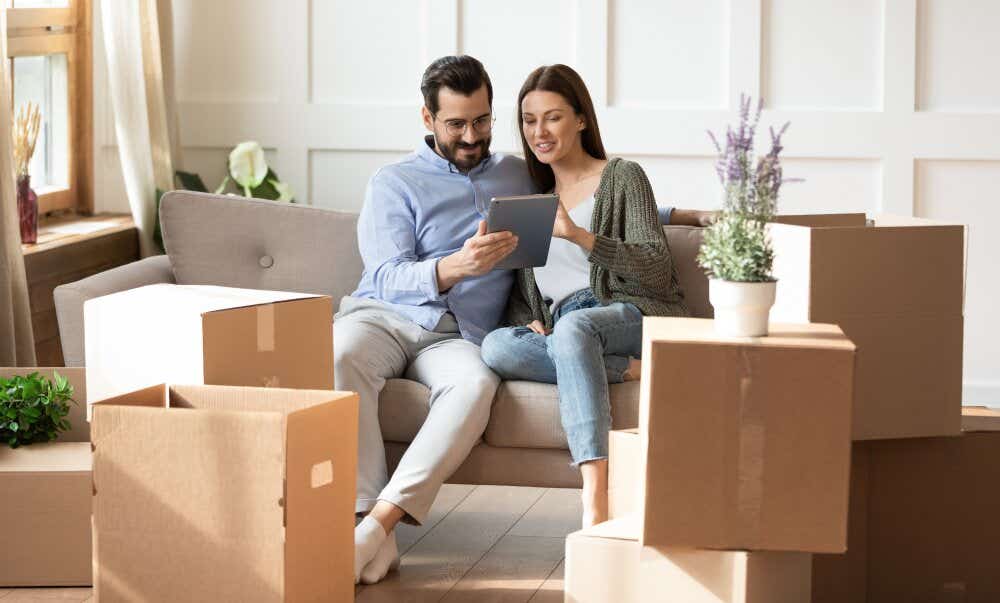 An image of a couple surrounded by boxes in their living room and researching on a tablet in preparation for moving house.