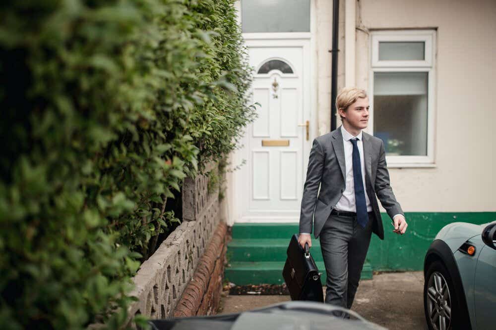 Young adult male walking you the house to go to the car to drive to work. He is dressed in a suit and tie and holding a breifcase.