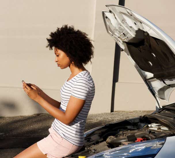 Woman leaning on her car and looking at her phone