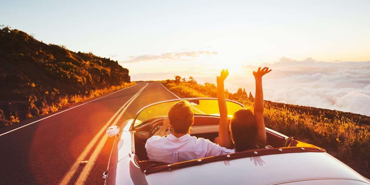 Couple in a car driving into sunset on holiday abroad