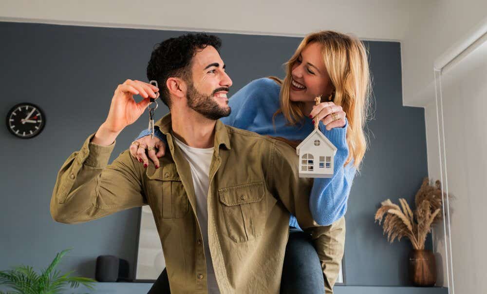 An image of a smiling couple holding a model house and house keys while celebrating moving house.