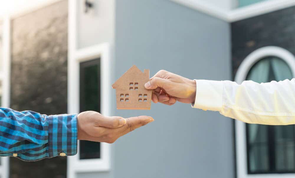 An image of a man handing over a model home to another man outside a house.