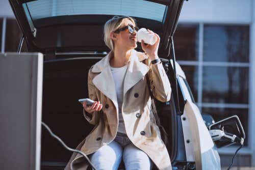 Woman charging car and drinking coffee