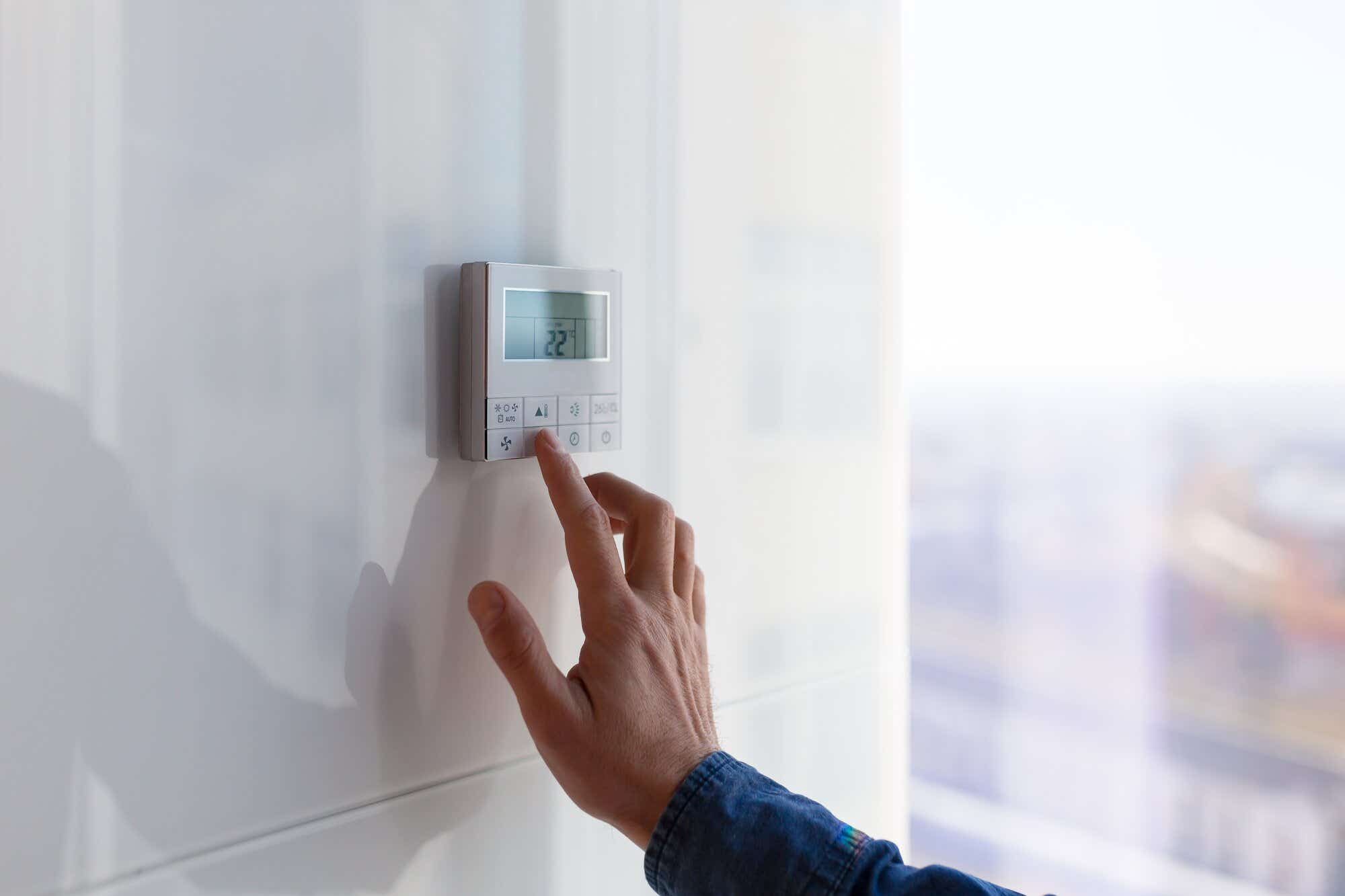 man touching heating control panel in apartment