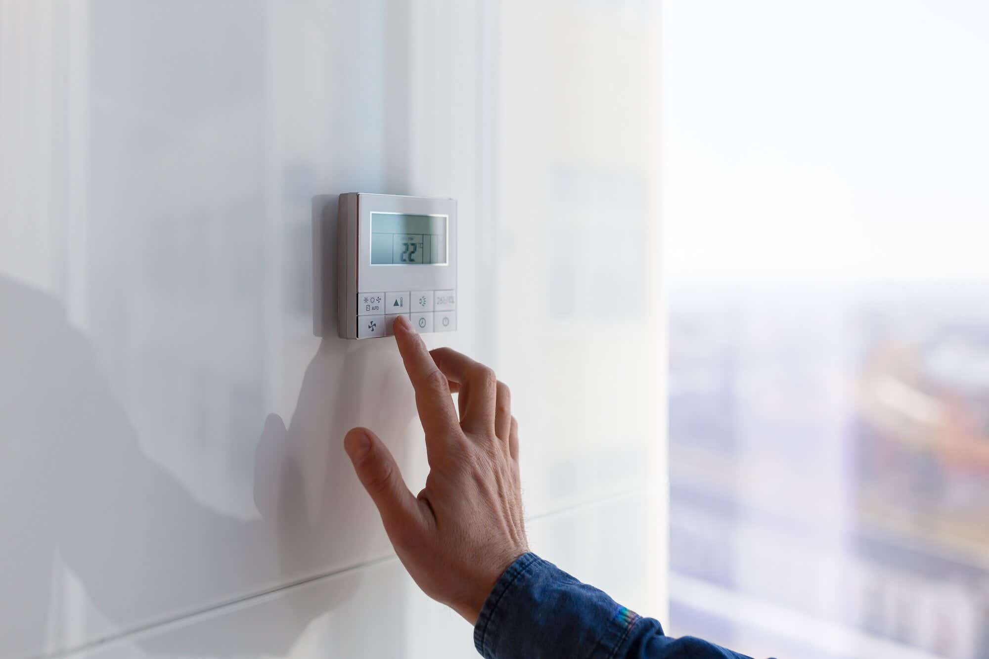 person pressing heating control panel on apartment wall 