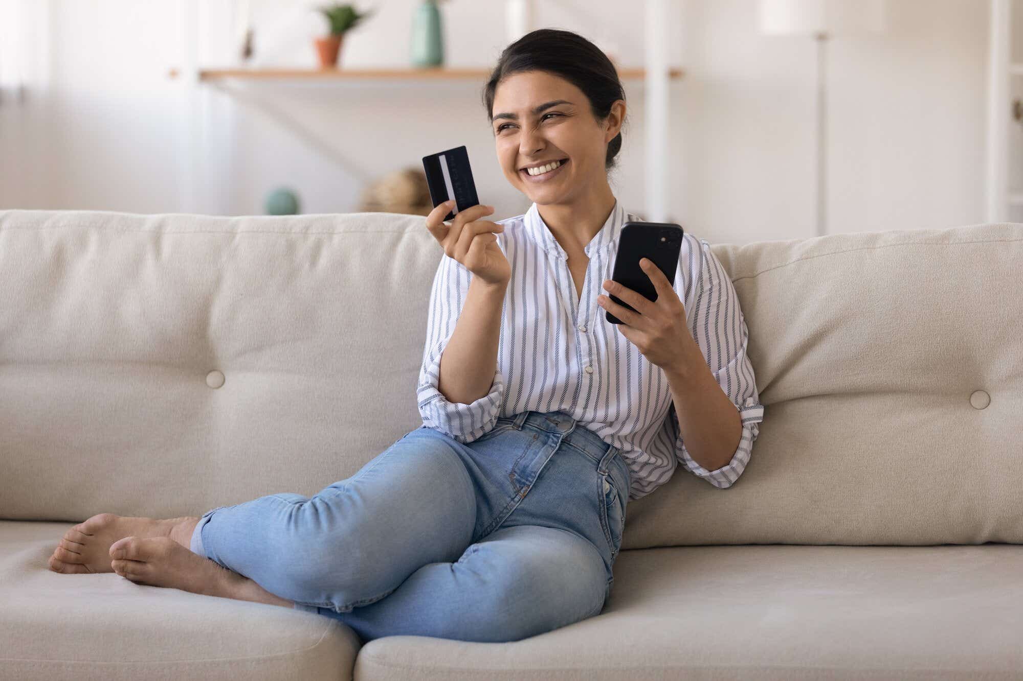 Person looking down at a phone in their hand while smiling and holding a credit card in the other hand