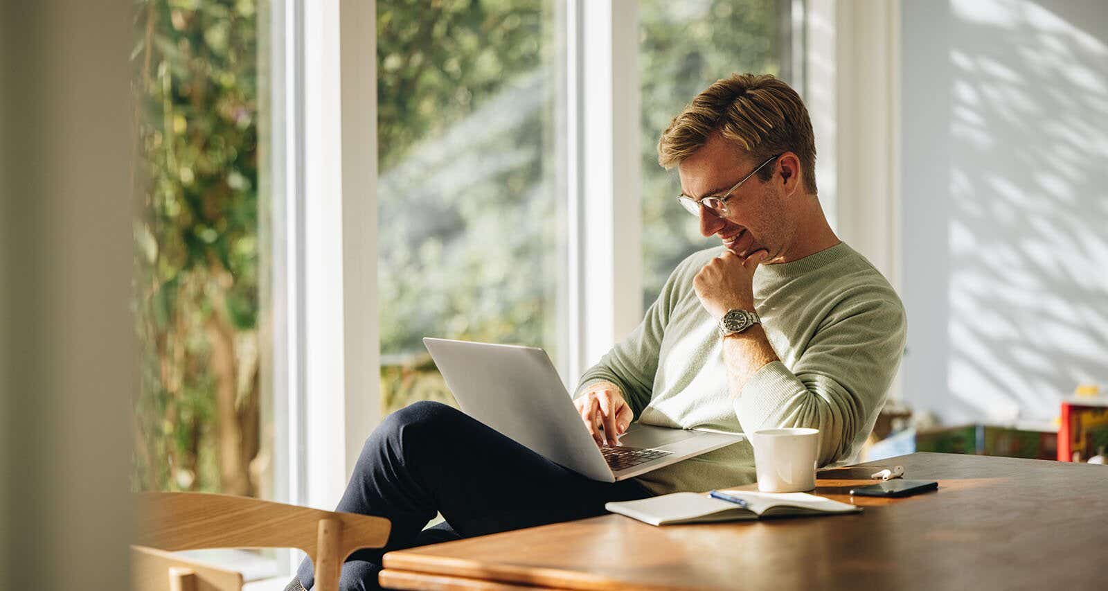 man smiling while sat at a table and working on his laptop