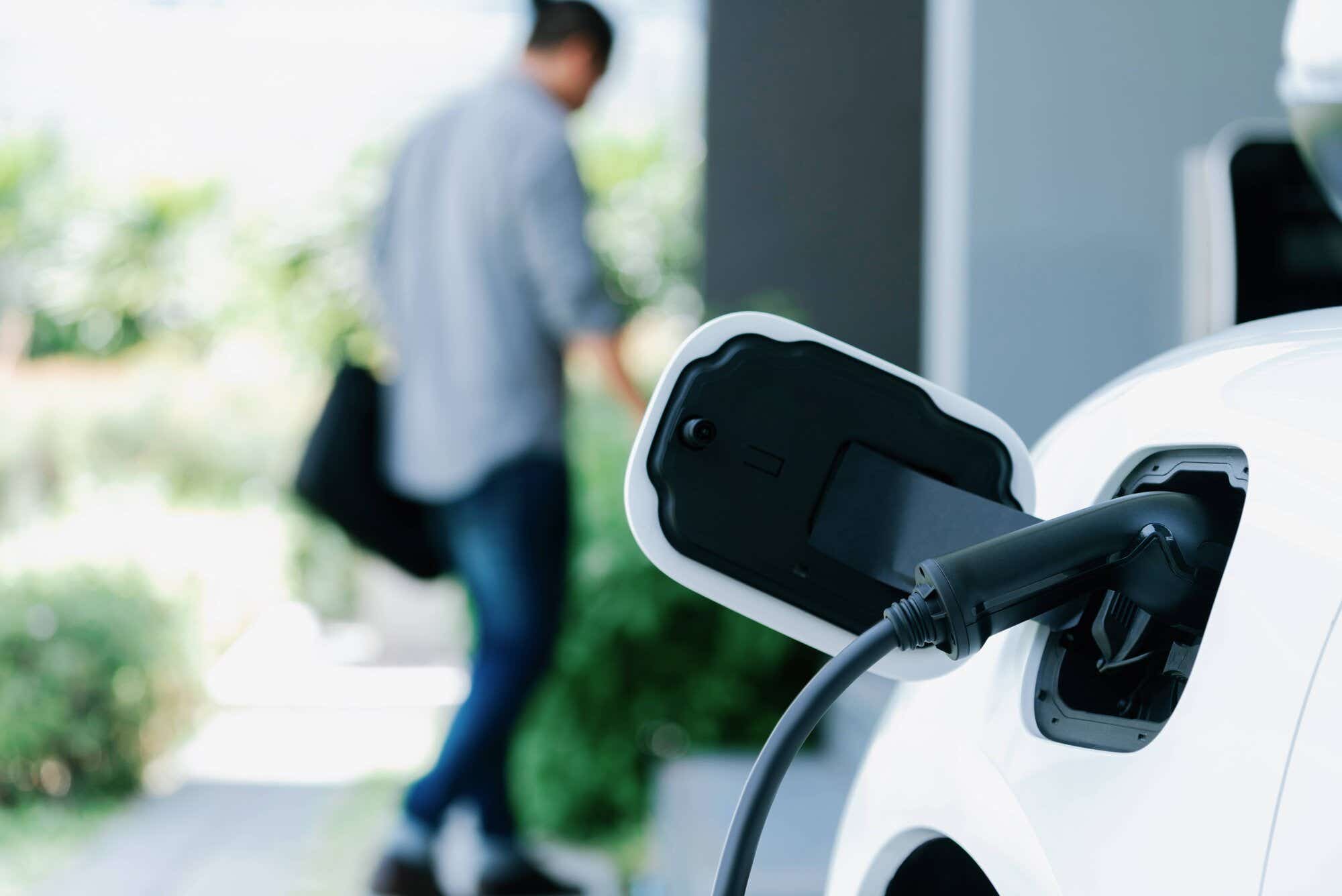 Close up of EV charger plugged into white car as a person walks away