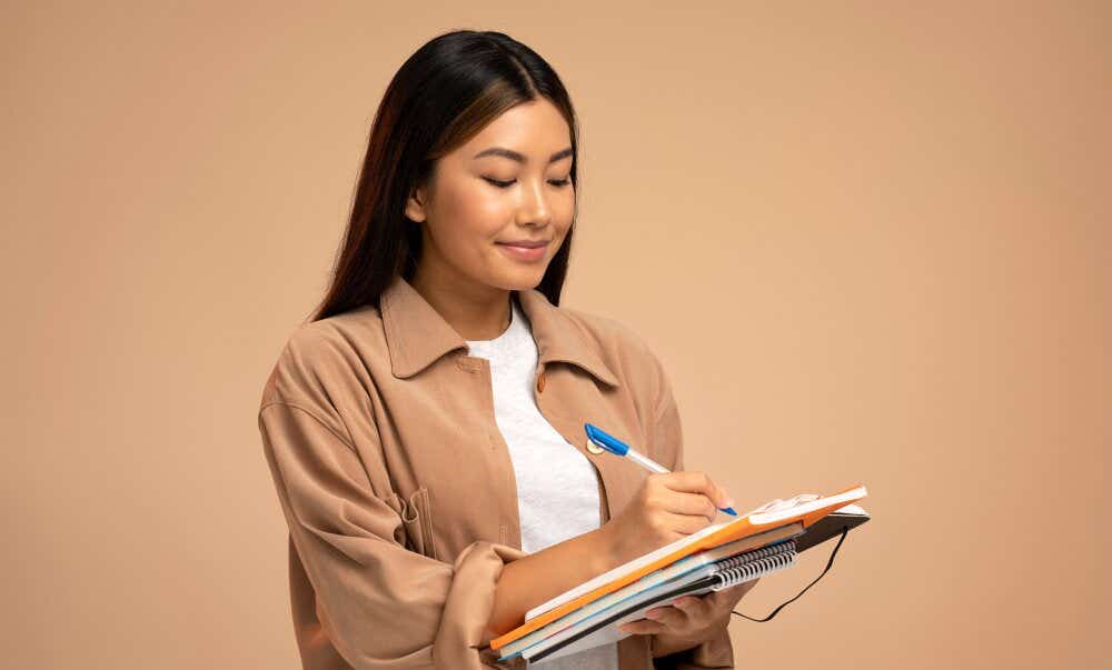 An image of a smiling woman writing on a notepad