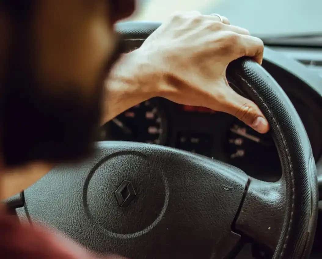 Looking over the shoulder of a driver with their hand on the steering wheel of a car