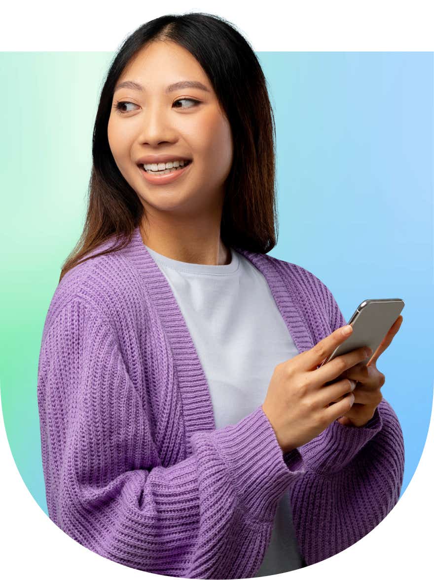 A woman smiles while holding her phone, looking off into the distance.