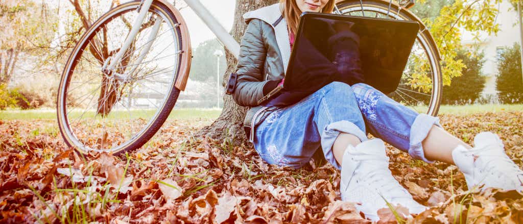Girl studying outside among leaves with laptop and bike