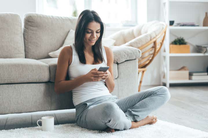 Young woman sitting on the floor at home checking her phone