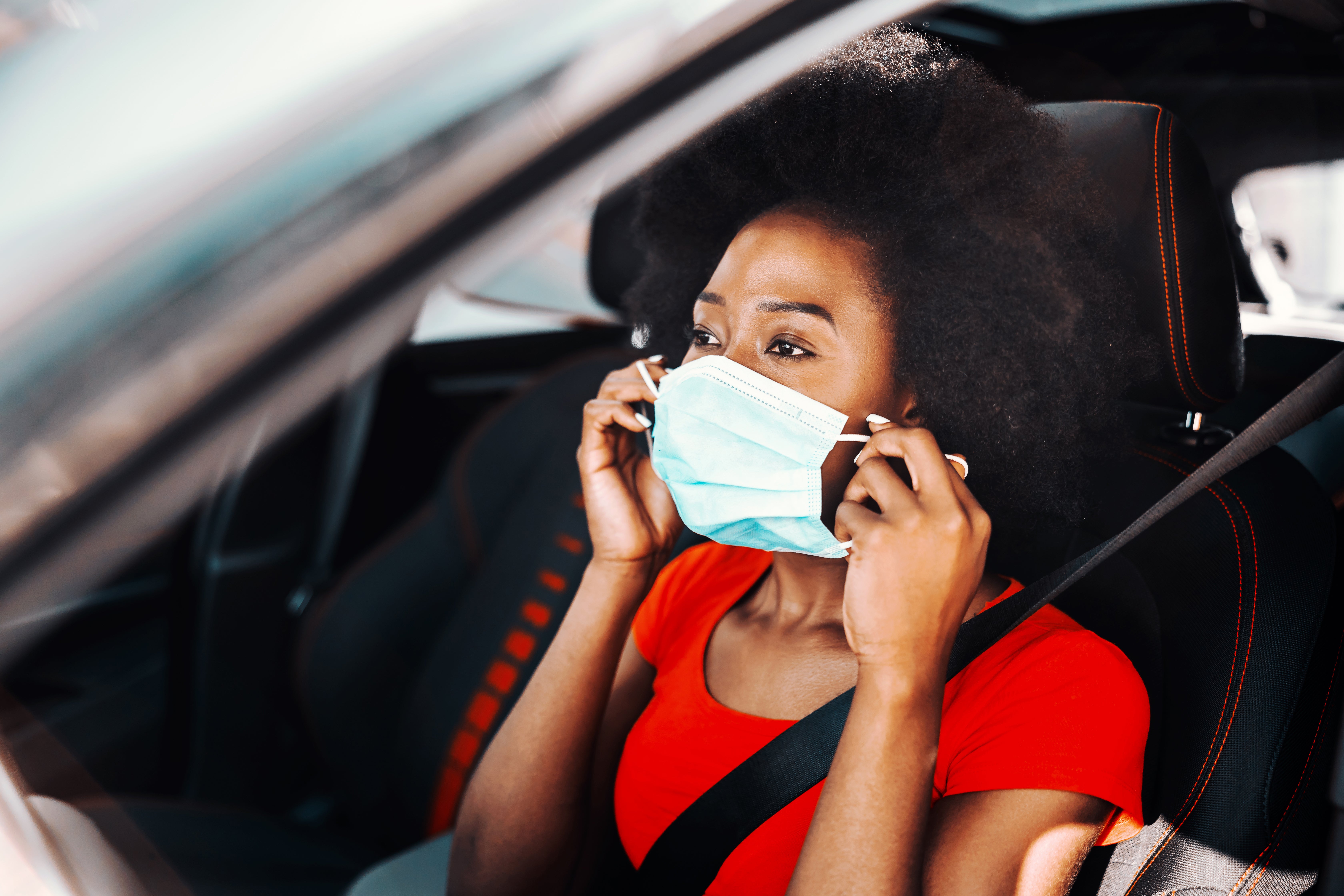 Mujer joven BAME con una máscara en un coche