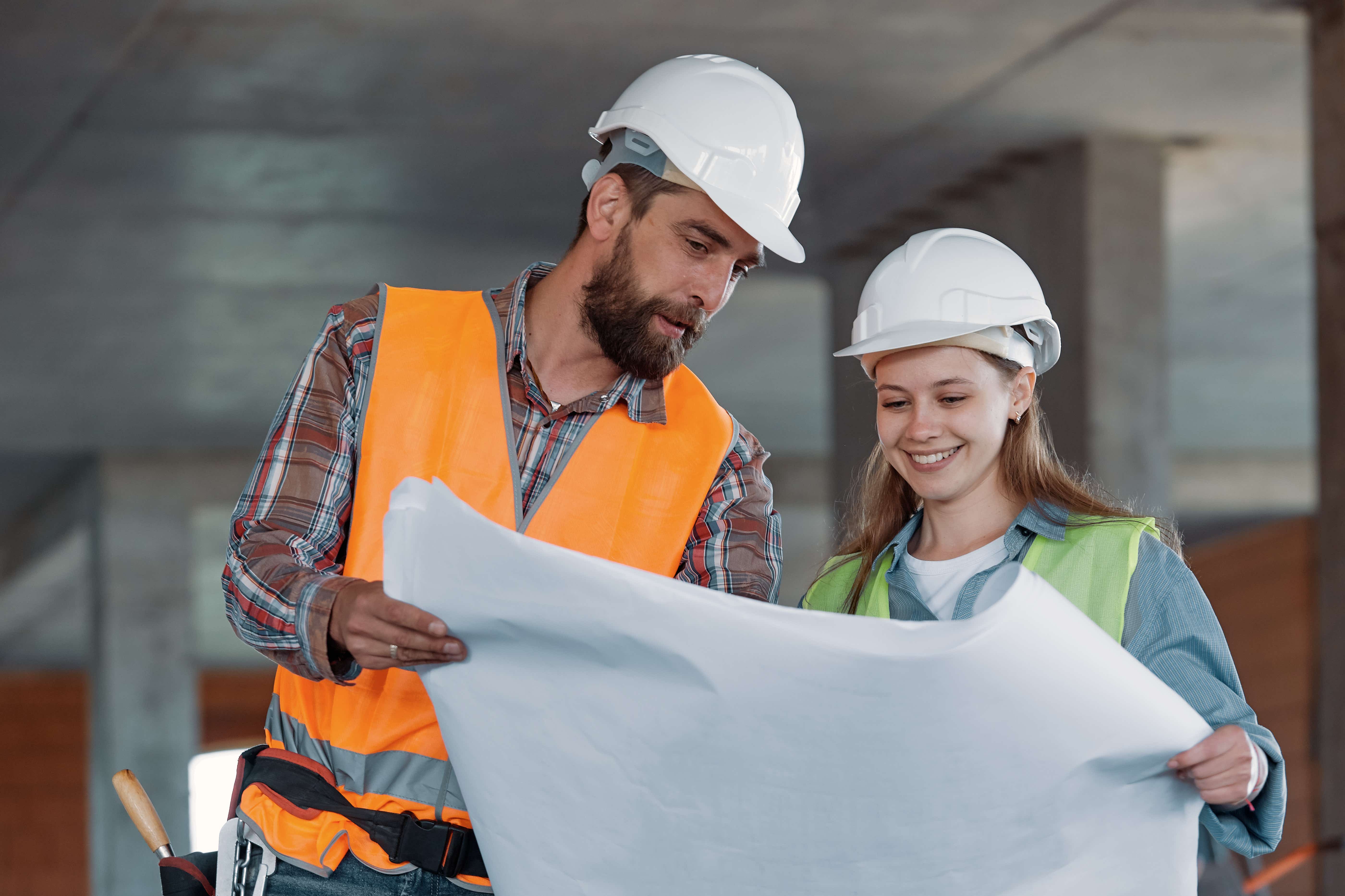Man and woman in hard hats look at a building plan