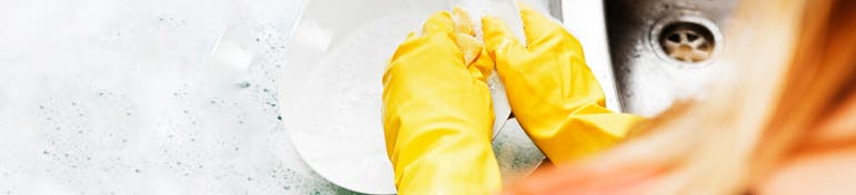 Person wearing rubber gloves washing up dishes by hand in sink