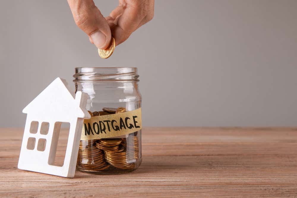 How to save for a mortgage deposit. Image of someone dropping coins in a jar labelled mortgage