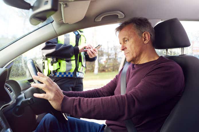 Police officer writing a ticket or issuing a fine to a male car driver