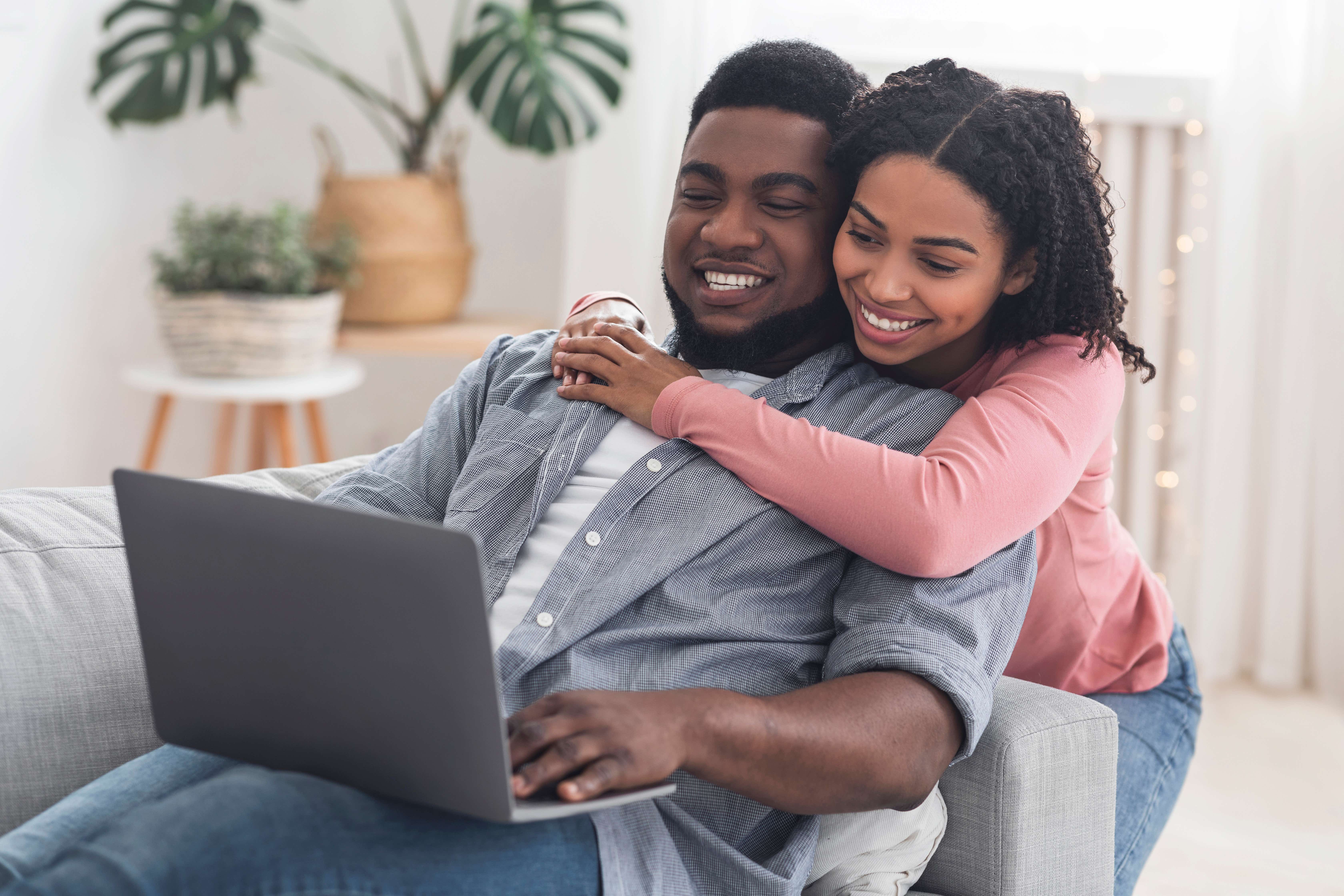 Couple hugging and smiling while looking at laptop