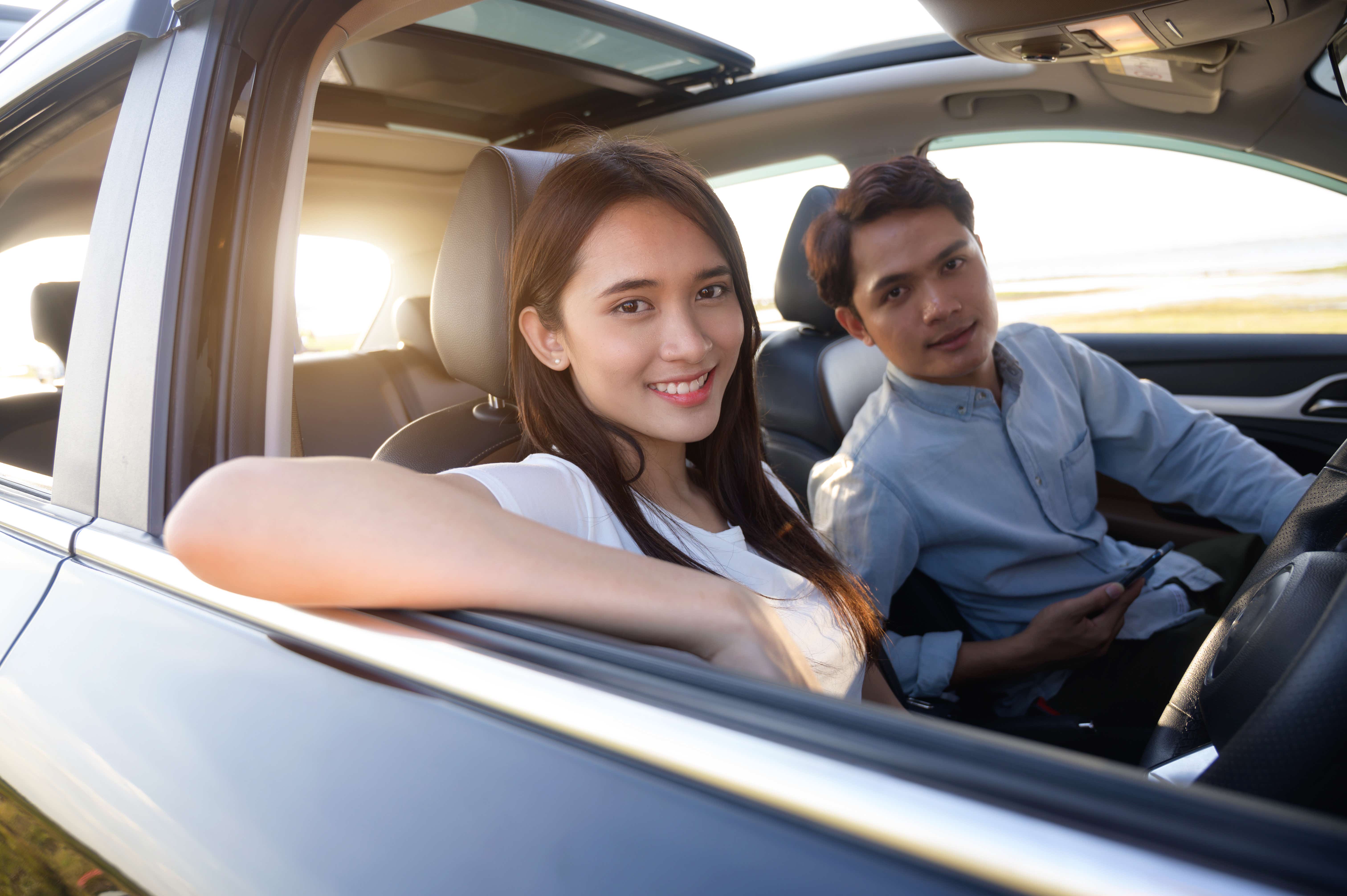 Young couple in his car, happy to drive on a country road. Happy young women and young men in car 
