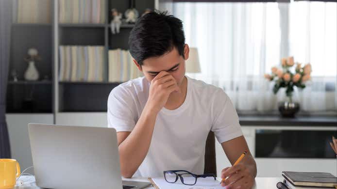 Asian man are tired and stressed about working on a laptop and taking notes at home.