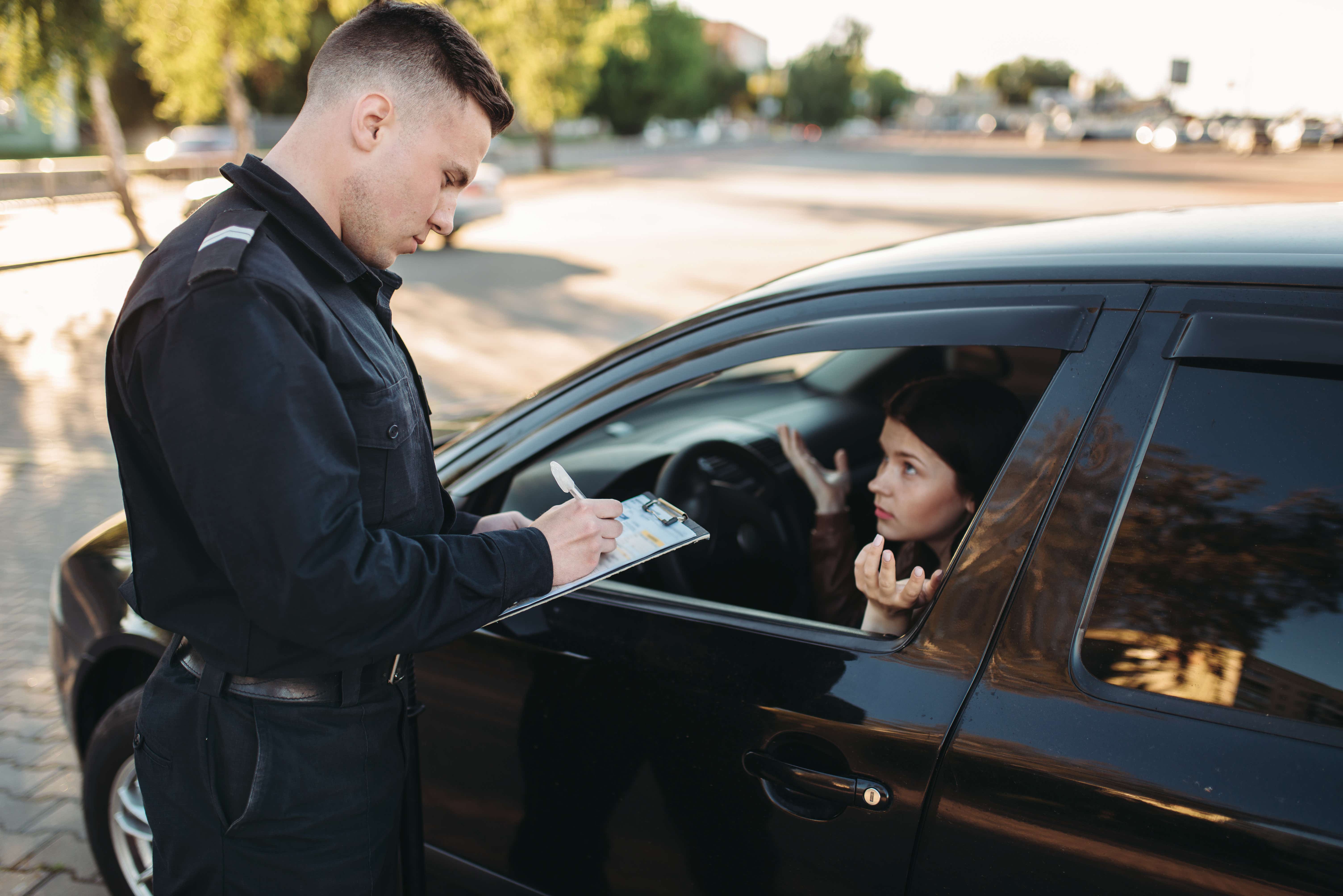Officer giving woman a ticket in a black car.