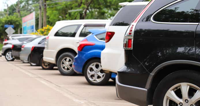 Closeup of rear side of black car and other parking in parking area beside the street with natural background in sunny day. 