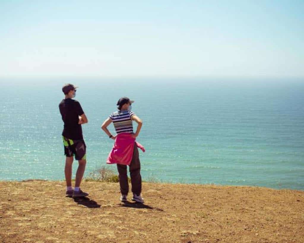 Man and woman looking around an empty beach wearing a facemask